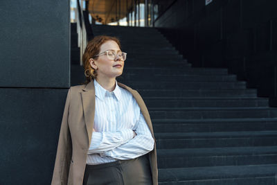 Young woman with eyes closed and arms crossed leaning on wall