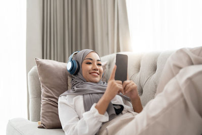 Young woman using mobile phone while lying on bed at home