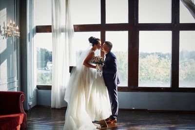 Side view of bride and bridegroom kissing against window