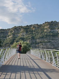 Rear view of man walking on bridge towards mountain against sky
