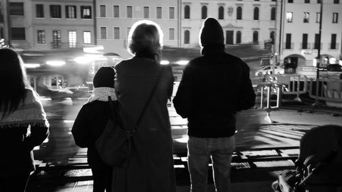 Rear view of people standing on street in city at night