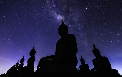 Low angle view of silhouette buddha statues against sky at night