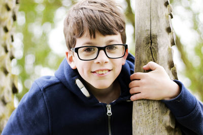 Portrait of boy wearing eyeglasses holding tree trunk