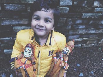 Boy holding puppets and standing against wall