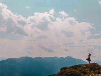 Woman doing yoga while standing on mountain against sky