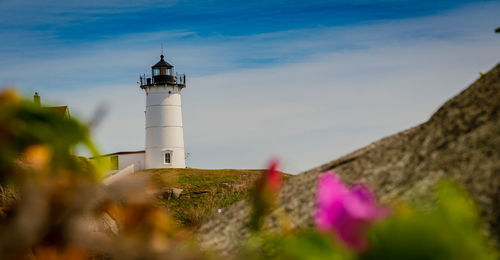 Lighthouse amidst plants and buildings against sky