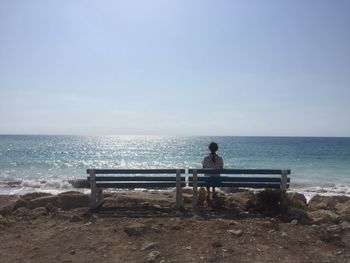 Man sitting on bench looking at sea against sky