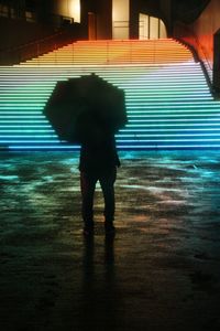 Silhouette of person walking on wet street at night