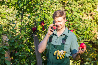 Young man using mobile phone while standing against plants