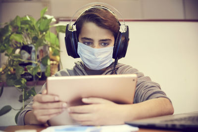 Boy wearing mask using digital tablet on table at home