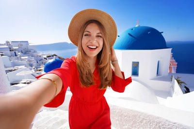 Happy young woman takes selfie photo between oia famous blue domes churches on santorini island.