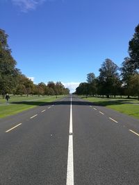 Empty road along trees and against blue sky