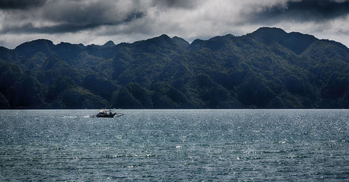 Sailboat sailing on sea by mountains against sky