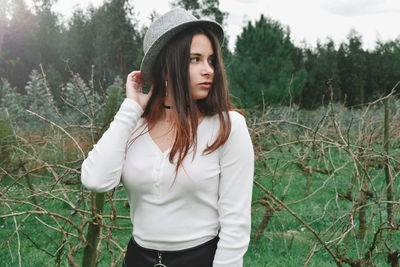 Beautiful woman looking away while standing against plants on field