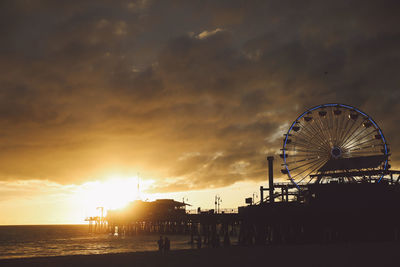 Silhouette santa monica pier against cloudy sky during sunset