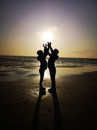 Silhouette people at beach against sky during sunset