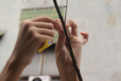 Cropped hands of person tying rolled paper with thread on stick