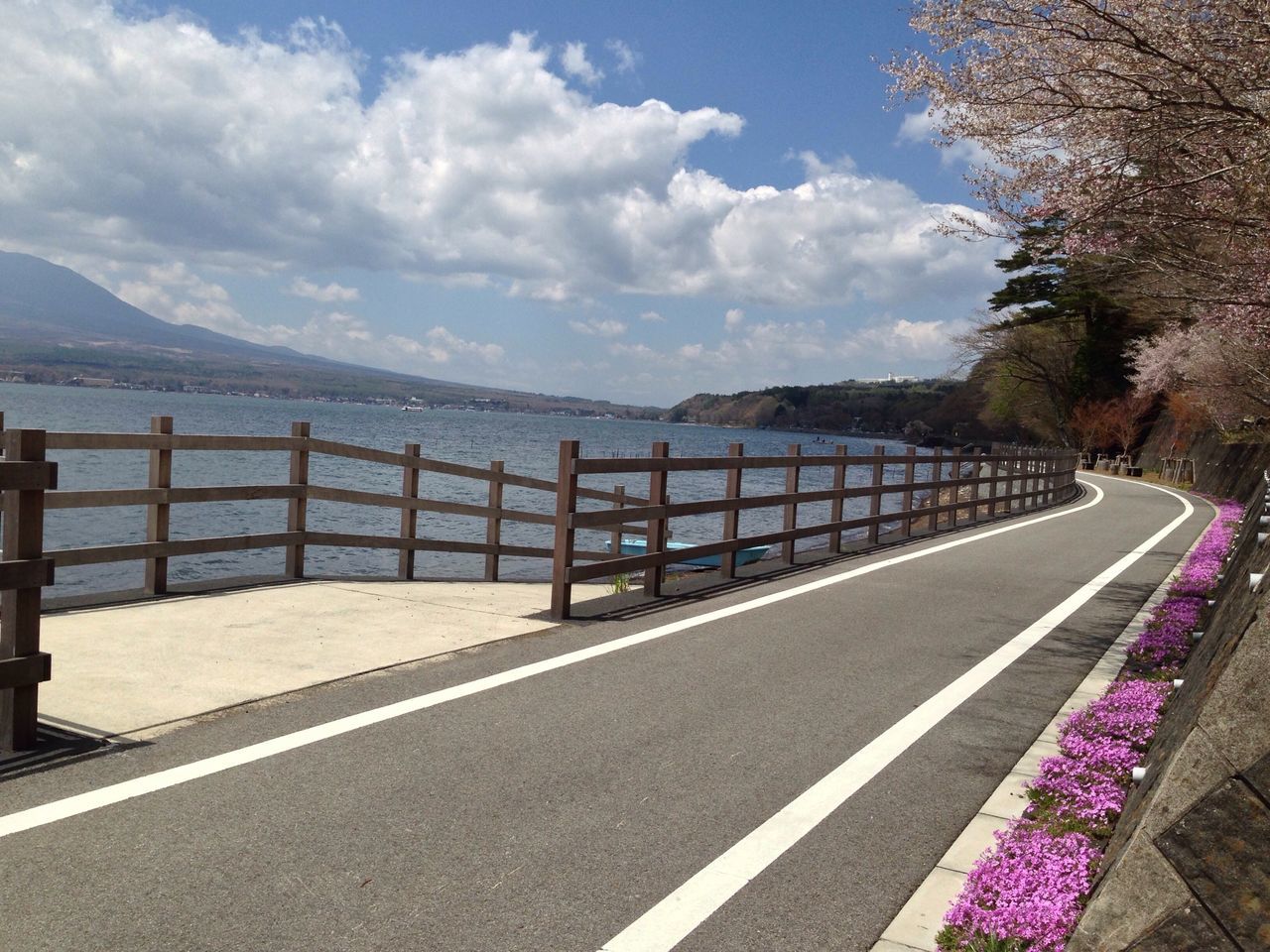 sky, railing, cloud - sky, sea, water, tranquil scene, tranquility, the way forward, road, nature, scenics, beauty in nature, cloud, mountain, empty, tree, sunlight, day, built structure, footpath