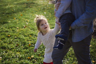 A little girl reaches up to hold her baby brother's hand