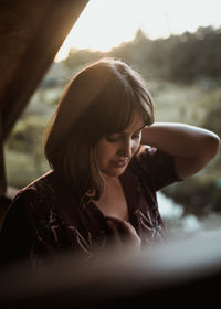 Portrait of young woman on ledge of wooden cabin at sunset