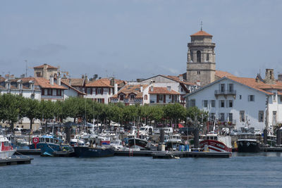 Sailboats in river by buildings in city against sky