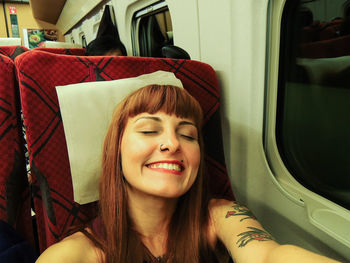 Self-portrait of a young traveler with red straight hair smiling with eyes closed inside of a train