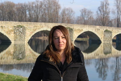 Portrait of woman standing by lake against bridge