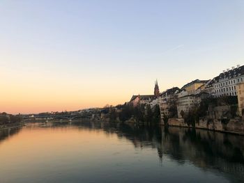 Buildings by river against clear sky during sunset