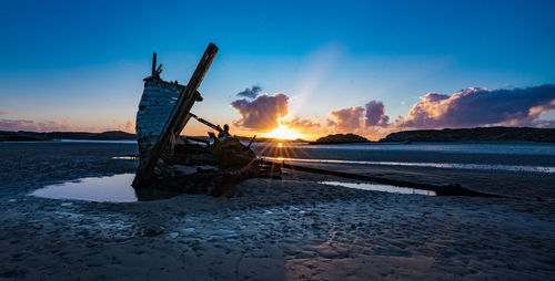 Abandoned boat at beach against sky during sunset