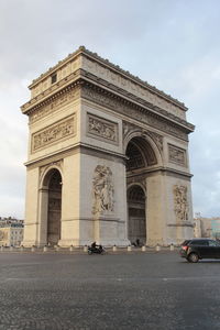 Low angle view of arc de triomphe by road against sky