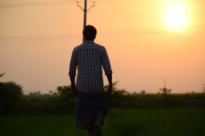 Rear view of man standing on field against sky at sunset