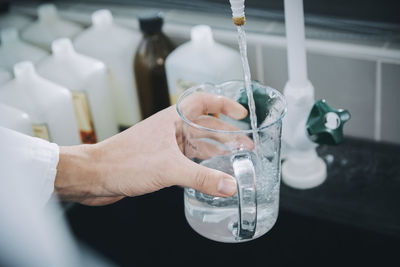 Cropped hand of female student filling beaker with liquid solution in chemistry laboratory