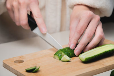 Close-up of female hands cutting fresh cucumbers on a wooden cutting board