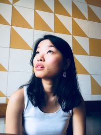 Beautiful woman looking away while sitting against wall