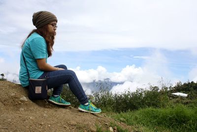 Side view of sad woman sitting on mountain against sky