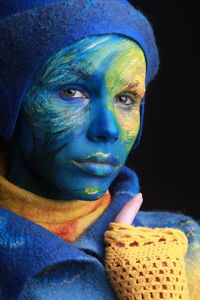 Portrait of young woman with painted face against black background