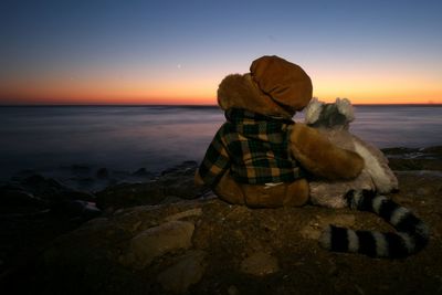 Stuffed toys at beach against sky during sunset