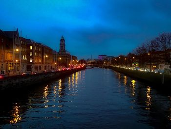 Illuminated buildings by river against sky at night