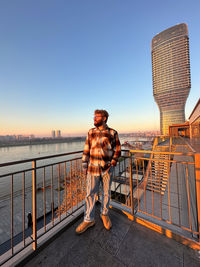 Rear view of man standing on bridge against clear sky during sunset