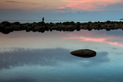 Silhouette man fishing in sea against sky during sunset