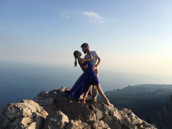 Romantic couple standing on mountain against sky