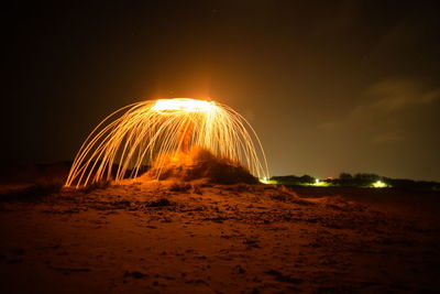 Illuminated light trails on beach against sky at night
