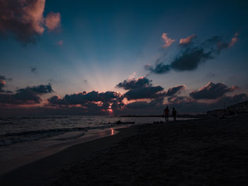 Silhouette people on beach against sky during sunset