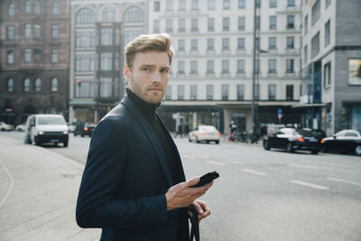 Side view of entrepreneur with phone standing against building in city