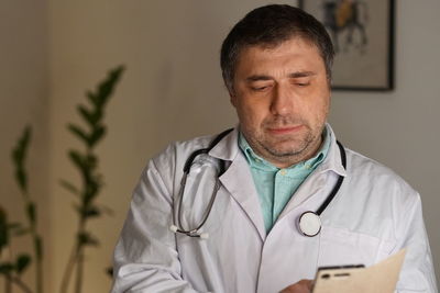 Close-up of mature doctor using phone against wall