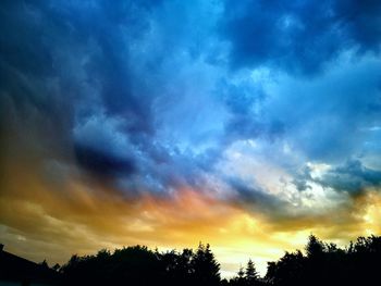 Low angle view of silhouette trees against dramatic sky