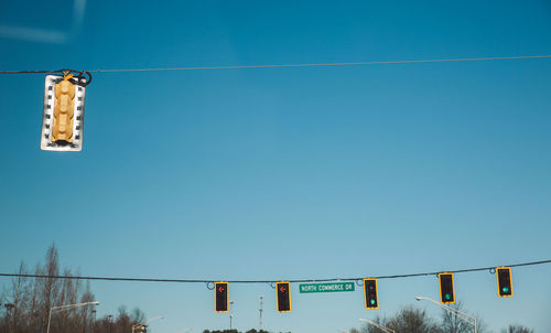 Low angle view of road signals hanging from cables against sky