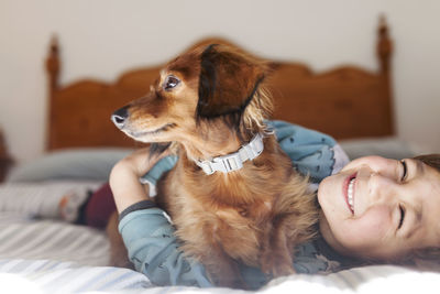 Smiling little boy lying on bed with long-haired dachshund