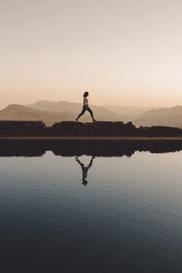 Side view of woman reflecting on lake against clear sky during sunset