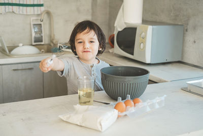 A little boy with a kitchen whisk in his hands plays near the table.